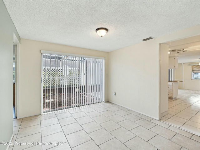 empty room featuring light tile patterned floors, baseboards, visible vents, and a textured ceiling