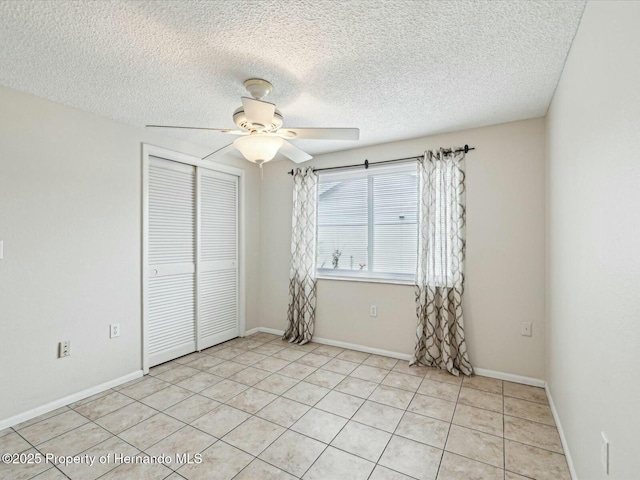 spare room with a textured ceiling, light tile patterned flooring, baseboards, and ceiling fan