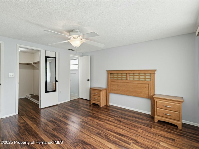 unfurnished bedroom featuring a spacious closet, baseboards, a closet, a textured ceiling, and dark wood-style flooring