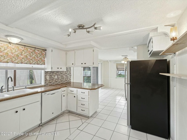 kitchen with a peninsula, light tile patterned flooring, white dishwasher, and freestanding refrigerator