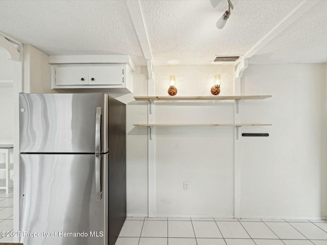 kitchen featuring visible vents, a textured ceiling, white cabinetry, freestanding refrigerator, and light tile patterned floors