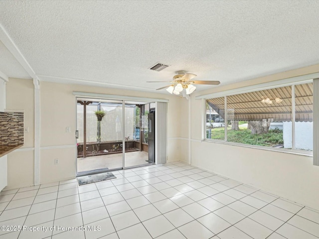 empty room featuring a textured ceiling, light tile patterned floors, visible vents, and ceiling fan