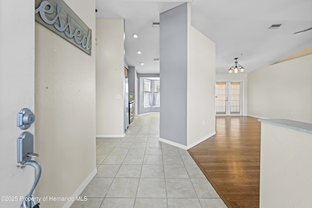 corridor featuring light tile patterned floors, visible vents, baseboards, and a chandelier