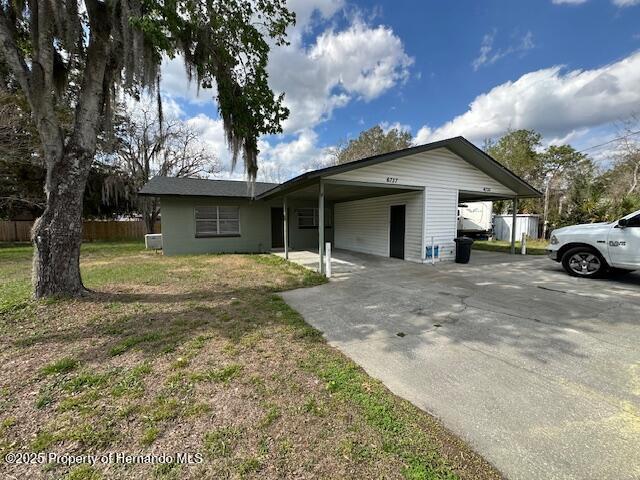 ranch-style house featuring an attached carport, concrete driveway, a front yard, and fence