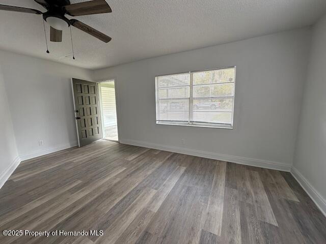 unfurnished room featuring dark wood finished floors, ceiling fan, a textured ceiling, and baseboards