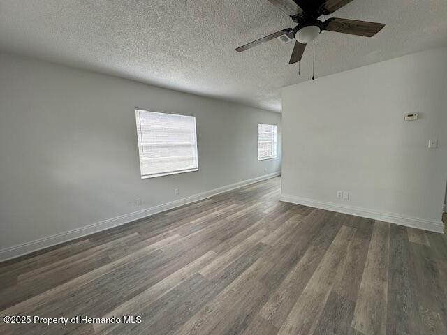 spare room featuring dark wood-style floors, a textured ceiling, baseboards, and a ceiling fan