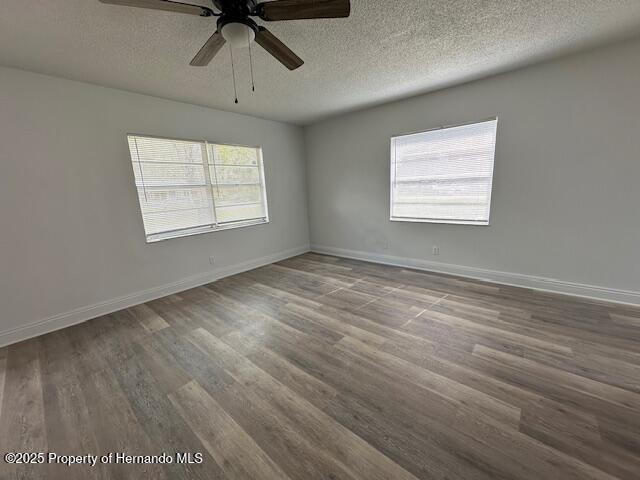 spare room featuring a wealth of natural light, a textured ceiling, baseboards, and wood finished floors