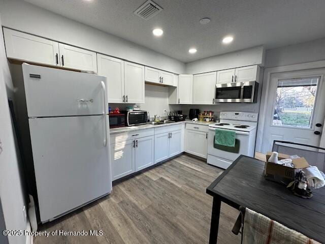 kitchen with visible vents, wood finished floors, recessed lighting, white appliances, and white cabinets