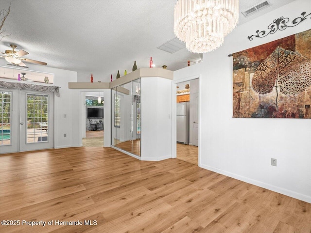 unfurnished living room with visible vents, french doors, a textured ceiling, ceiling fan with notable chandelier, and light wood-type flooring