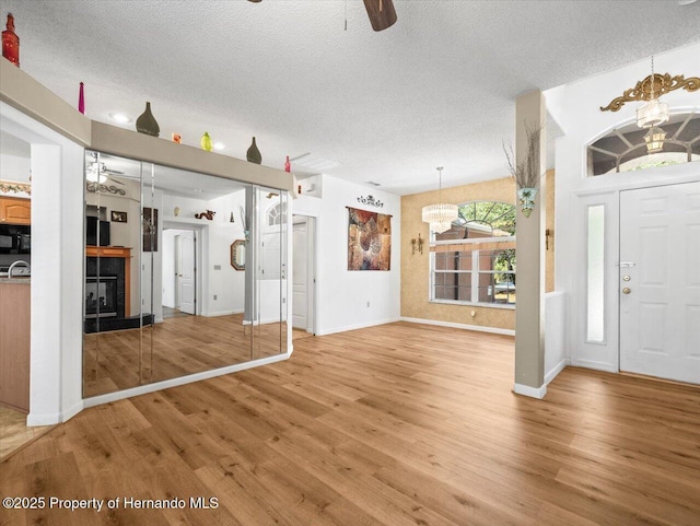 foyer entrance with light wood-type flooring, a textured ceiling, a glass covered fireplace, and ceiling fan with notable chandelier