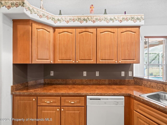 kitchen with dark countertops, a sink, a textured ceiling, and white dishwasher