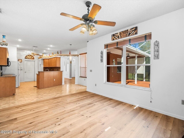 unfurnished living room with baseboards, a textured ceiling, ceiling fan, and light wood finished floors