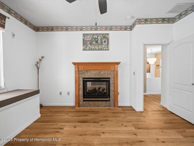 unfurnished living room featuring a ceiling fan, visible vents, a fireplace, a textured ceiling, and light wood-type flooring