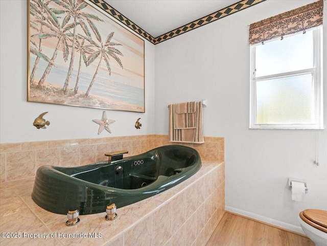 bathroom featuring toilet, wood finished floors, baseboards, and a whirlpool tub