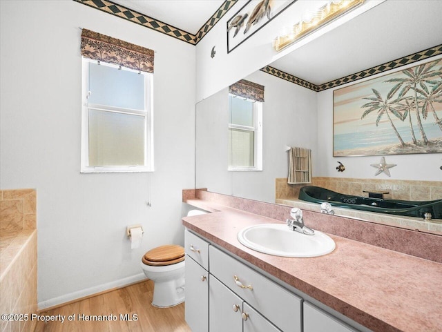 bathroom with baseboards, toilet, a tub to relax in, wood finished floors, and vanity