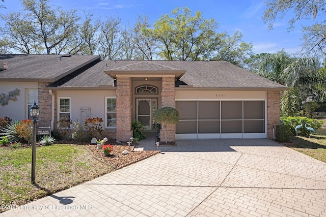 ranch-style home featuring stucco siding, decorative driveway, a shingled roof, a garage, and brick siding