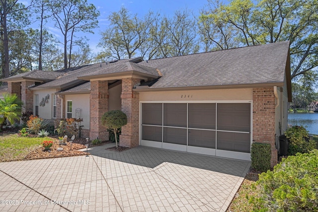 view of front of property with a garage, decorative driveway, brick siding, and roof with shingles