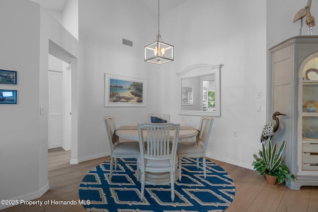 dining space with a notable chandelier, wood finished floors, visible vents, and a towering ceiling