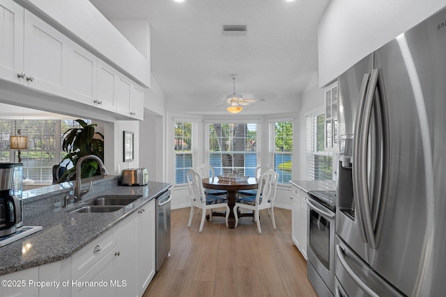 kitchen featuring light wood finished floors, lofted ceiling, dark stone countertops, appliances with stainless steel finishes, and a sink