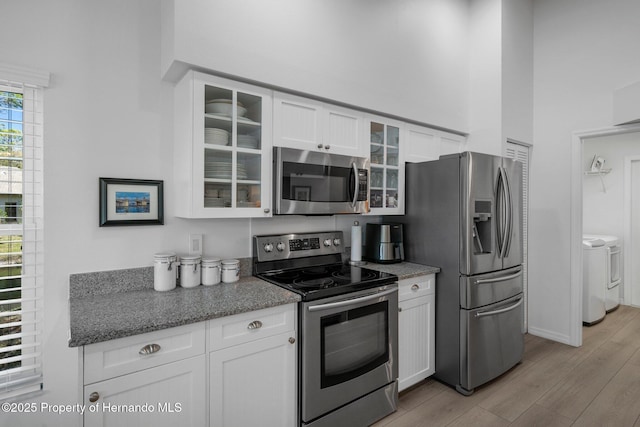 kitchen featuring light wood finished floors, glass insert cabinets, appliances with stainless steel finishes, white cabinetry, and separate washer and dryer