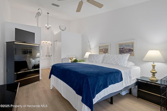 bedroom with wood finished floors, visible vents, lofted ceiling, ensuite bathroom, and a chandelier