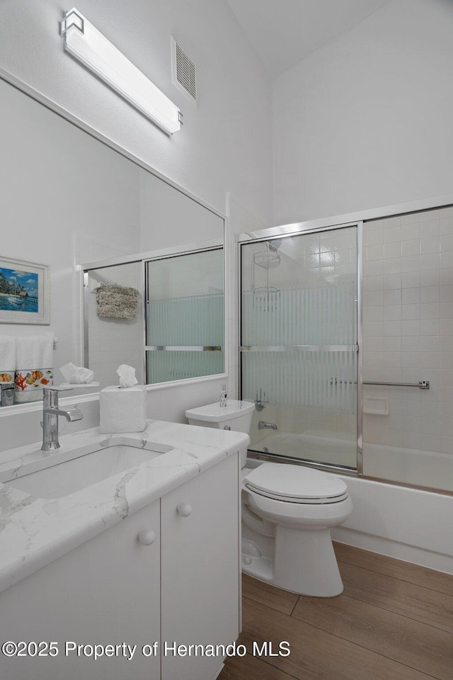 bathroom with visible vents, toilet, wood finished floors, shower / bath combination with glass door, and vanity