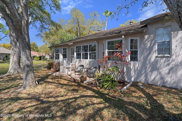 back of property with stucco siding, a patio, and a lawn