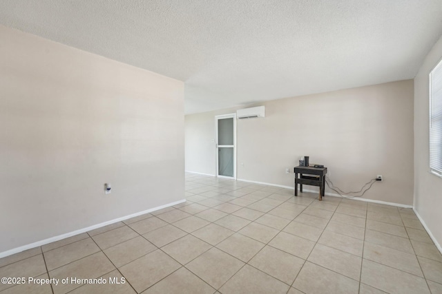 spare room with a wall mounted air conditioner, baseboards, a textured ceiling, and light tile patterned floors