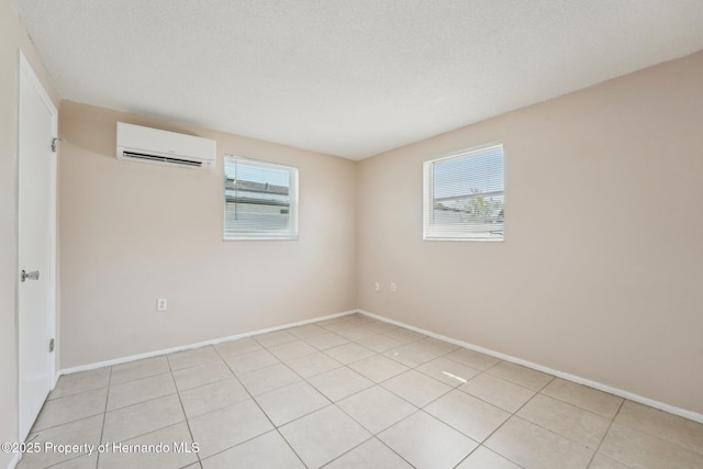 empty room featuring a healthy amount of sunlight, baseboards, a wall mounted air conditioner, and a textured ceiling