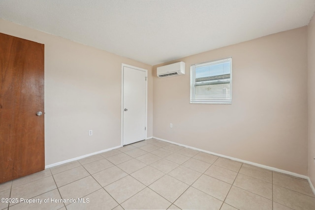 unfurnished room with light tile patterned flooring, an AC wall unit, and baseboards