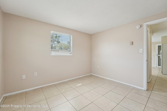 spare room with light tile patterned floors, baseboards, and a textured ceiling