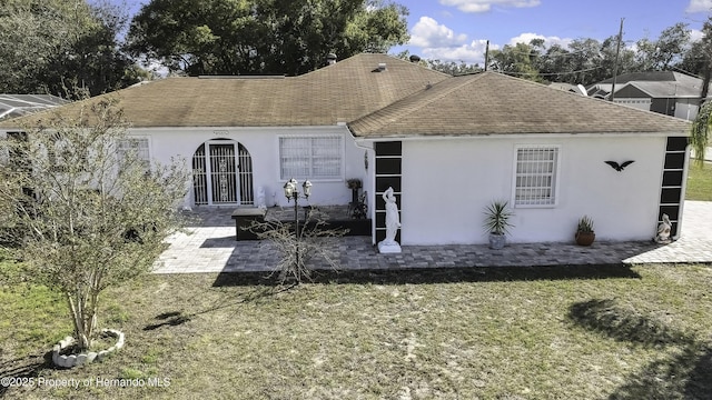 ranch-style house featuring stucco siding, roof with shingles, a front lawn, and a patio area