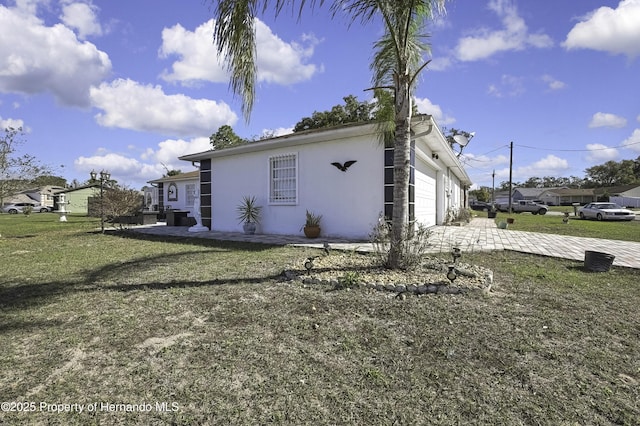 view of side of home with a yard, a garage, driveway, and stucco siding