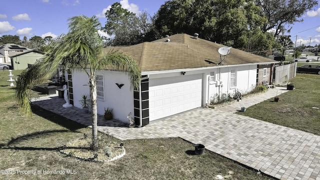 view of home's exterior with stucco siding, decorative driveway, a garage, and roof with shingles