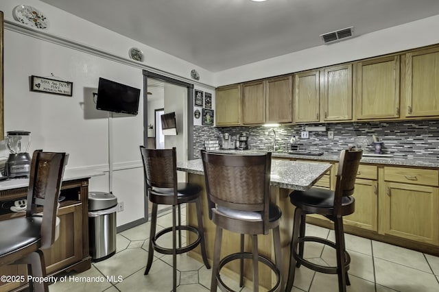 kitchen featuring visible vents, a kitchen breakfast bar, a kitchen island, light tile patterned floors, and decorative backsplash