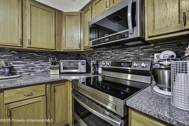 kitchen with dark stone countertops, stainless steel appliances, decorative backsplash, and a toaster