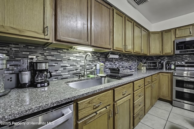 kitchen with tasteful backsplash, stone counters, appliances with stainless steel finishes, light tile patterned flooring, and a sink