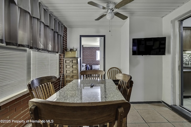 dining area featuring light tile patterned flooring, a ceiling fan, baseboards, and brick wall