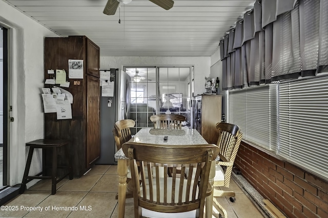 dining space with light tile patterned floors, brick wall, and ceiling fan