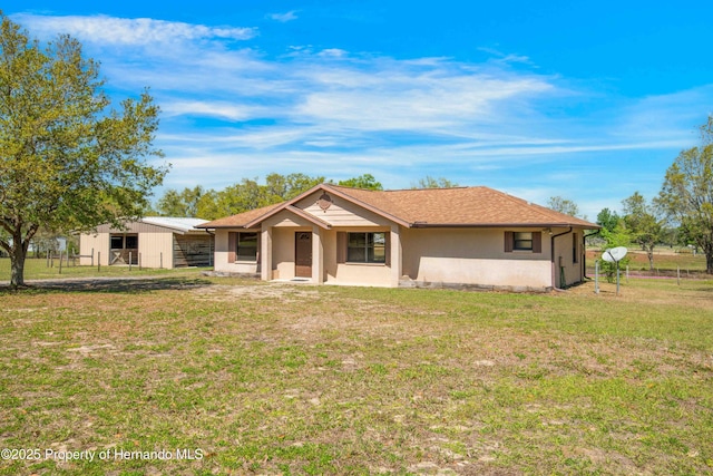 ranch-style home with stucco siding, an outdoor structure, a front yard, and fence