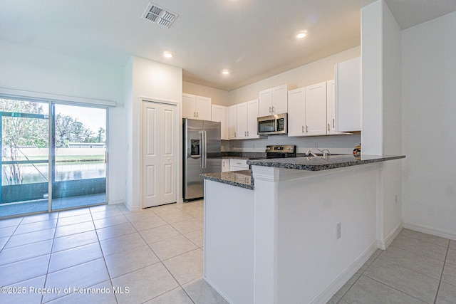 kitchen featuring visible vents, dark stone counters, appliances with stainless steel finishes, a peninsula, and white cabinetry