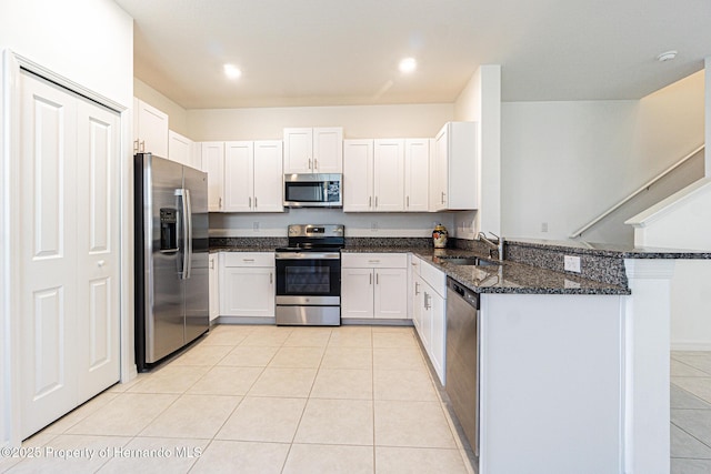 kitchen with a sink, dark stone counters, appliances with stainless steel finishes, a peninsula, and light tile patterned floors