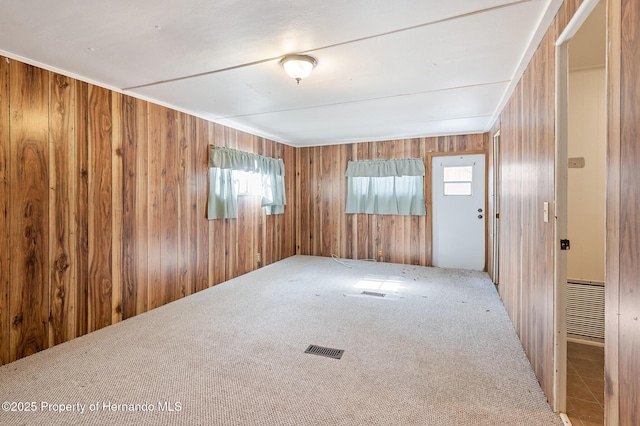 carpeted spare room with wooden walls and visible vents