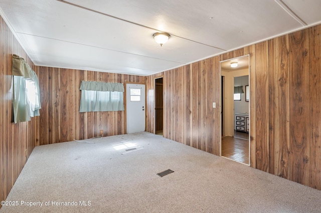 unfurnished room with visible vents, wooden walls, and carpet