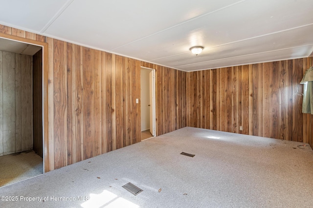 empty room featuring wooden walls, visible vents, and carpet floors