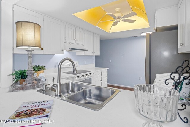 kitchen featuring under cabinet range hood, light countertops, freestanding refrigerator, white electric range oven, and a sink