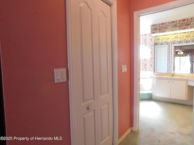 hall featuring wallpapered walls, light colored carpet, baseboards, and a sink