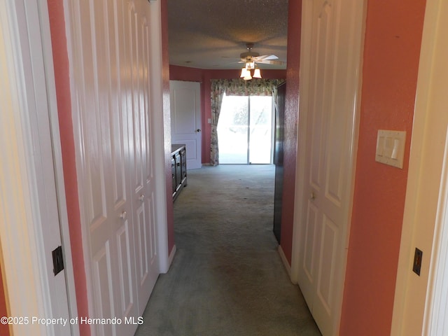 corridor with a textured ceiling, baseboards, and carpet floors