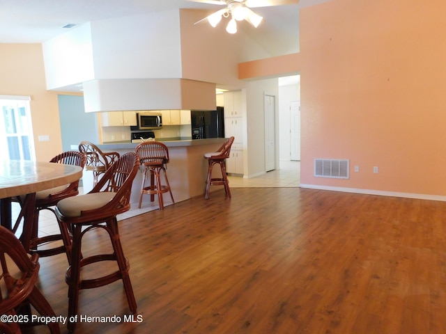 dining space featuring visible vents, high vaulted ceiling, light wood-style floors, and a ceiling fan