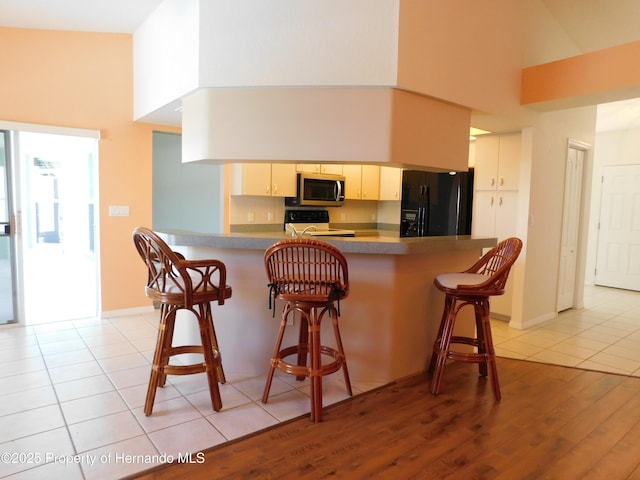 kitchen with stainless steel microwave, a high ceiling, black fridge, and electric range oven